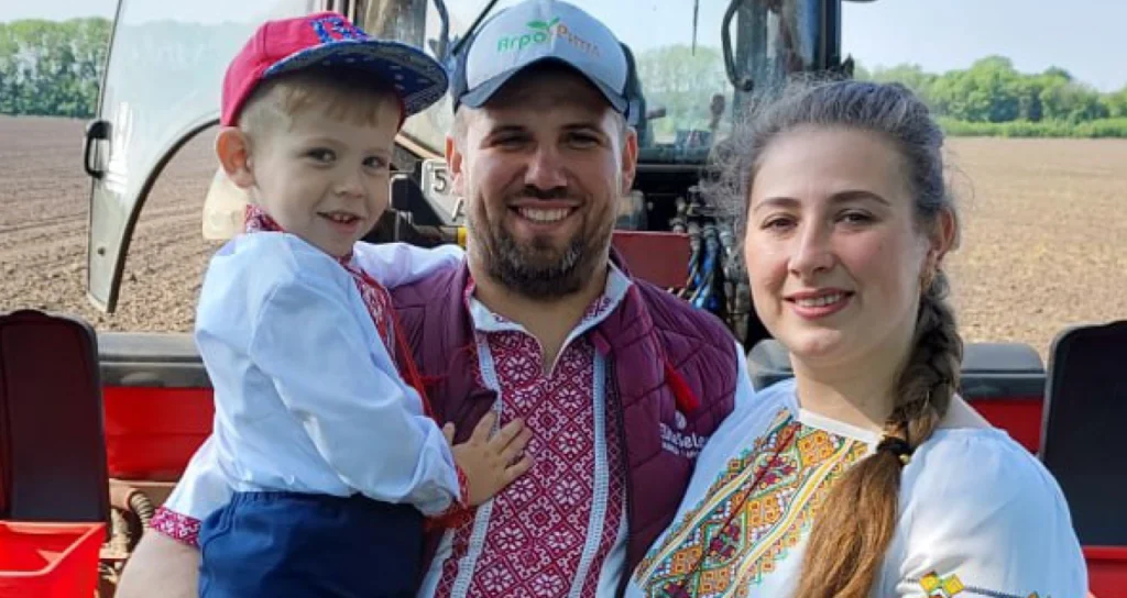 Сім'я в українських вишиванках стоїть перед трактором на полі.
